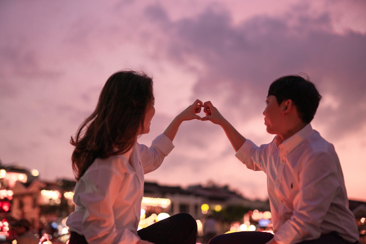 Romantic couple creating a heart with hands during a beautiful sunset.