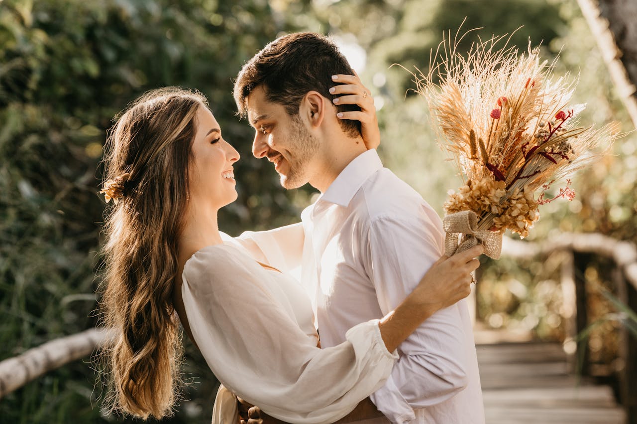 Side view of delightful newlyweds hugging and looking at each other while standing outside on blurred background